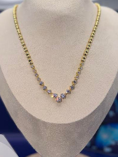 A gold chain necklace with a V-shaped pendant set with small blue and clear stones, displayed on a beige jewelry bust. A branded card for 'Ayu Boutique' is visible in the lower left corner.
